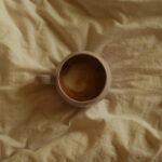 Aerial view of a coffee mug with frothy drink resting on a soft beige fabric, creating a warm and cozy ambiance.