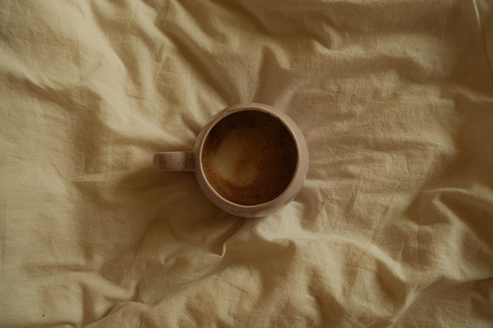 Aerial view of a coffee mug with frothy drink resting on a soft beige fabric, creating a warm and cozy ambiance.